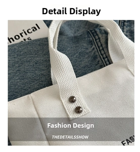 Detailed close-up of white canvas tote bag with woven handles and metallic rivet accents