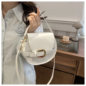 Close-up of white saddle bag with gold metal buckle held in a cozy indoor setting