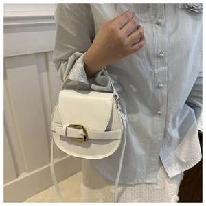 Detail of white saddle bag with gold buckle closure and sleek synthetic leather texture