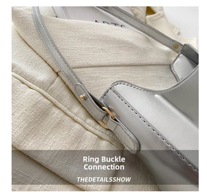 Detailed close-up of golden metal buckle and stitching on silver leather shoulder bag