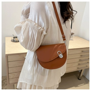 Detail of brown saddle crossbody bag featuring silver oval metal twist lock and leather texture