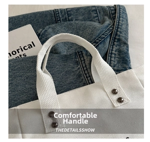 Close-up of white canvas tote bag with metal rivets and sturdy handle stitching