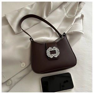 Detail of a dark brown underarm bag with a large rhinestone buckle on a satin fabric