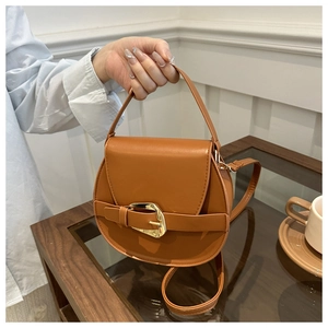 Detail of a brown semi-circle leather bag showing golden metal buckle and smooth matte finish