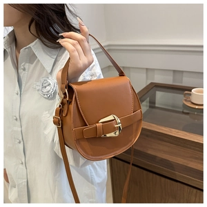 Brown leather saddle bag with gold buckle detail shown in a lifestyle setting
