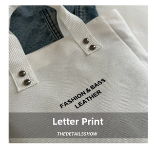 Macro detail of white canvas tote bag featuring black lettering and retro metal rivets