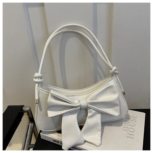 Detail of white glossy shoulder bag featuring a large bow and twisted rope handle