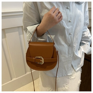 Brown leather saddle bag with gold buckle shown worn as a crossbody on a model