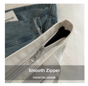 Close-up of smooth silver metal zipper and black lining on white canvas tote bag