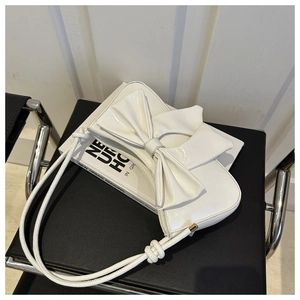 Detailed view of white patent leather shoulder bag with large decorative bow and knot strap
