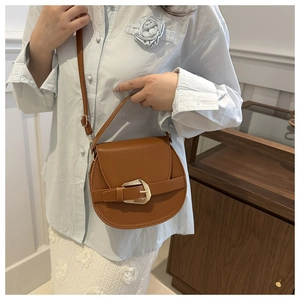 Detail of a brown leather saddle bag with gold horseshoe buckle worn across the shoulder
