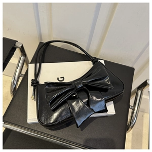 Detail of glossy black underarm bag with a large decorative bow on a leather surface