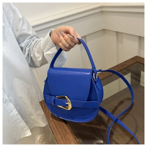 Detail of blue saddle bag featuring golden horseshoe buckle and matte leather texture