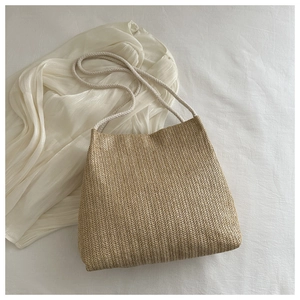 Detailed view of woven straw tote bag featuring herringbone texture and white rope handles