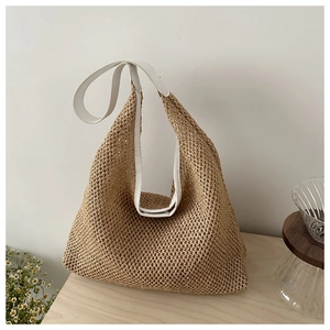Detail of woven straw tote bag with white leather trim on a minimalist wooden table