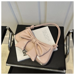 Close-up of a pale pink underarm bag with a large bow detail on a leather chair