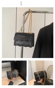 Detail of black faux leather bag with wavy stitching and gold chain strap