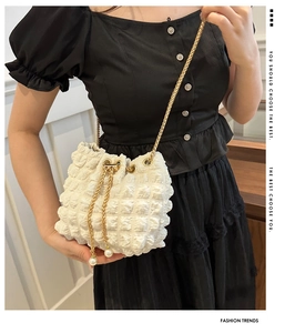 Detail of white pleated bucket bag with gold chain strap and pearl drawstring charms