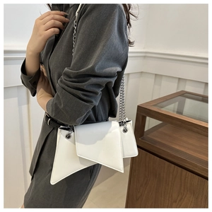 Gros plan d'un sac géométrique blanc avec chaîne argentée porté à l'épaule sur modèle