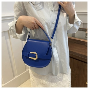 Detail view of cobalt blue saddle bag with golden horseshoe buckle and leather texture
