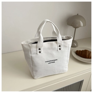 Détail du sac seau en toile blanche avec imprimé noir et poignées à rivets métalliques