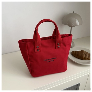 Détail du sac à main en toile rouge avec lettrage noir et rivets métalliques de renfort