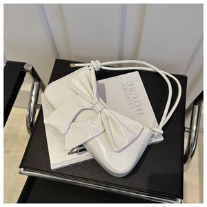 Close-up of white glossy shoulder bag with a large bow detail on a luxury magazine