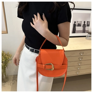 Detail of orange saddle bag with gold metal buckle shown in a lifestyle setting