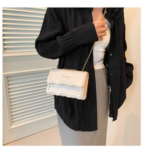Detail of a beige quilted crossbody bag with a gold chain strap worn by a model