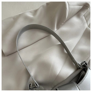 Detail of silver metallic shoulder bag showing fine stitching and polished metal ring buckle
