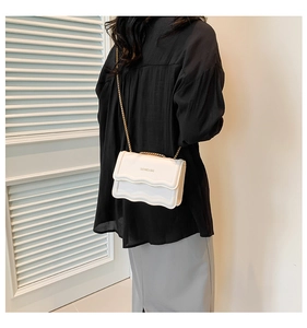 Detail of white crossbody bag with scalloped flap and gold chain strap on model