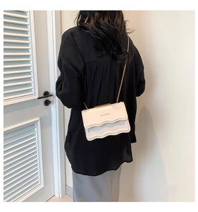 Detail shot of ivory crossbody bag with wave flap design and gold chain strap