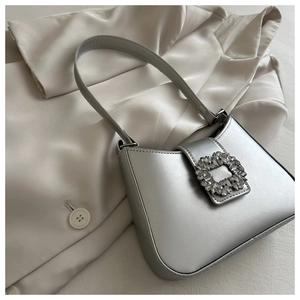 Detail of silver pearlescent underarm bag featuring a sparkling crystal buckle on silk blazer