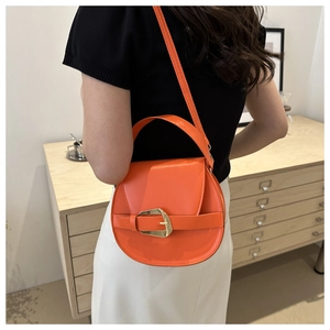 Close-up of vibrant orange saddle bag with gold buckle detail and glossy leather texture