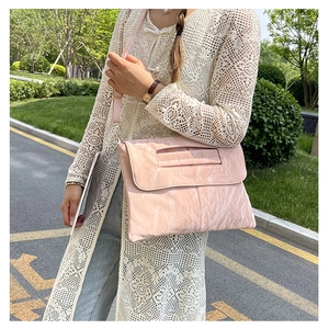 Pink patent leather crossbody bag with pleated texture shown on a model outdoors