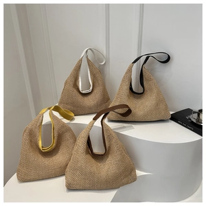 Close-up of bohemian woven straw tote bags in four strap colors on white pedestals