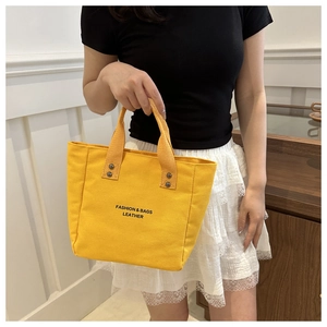 Détail d'un cabas en toile jaune avec texte mode et rivets sur fond en bois vintage