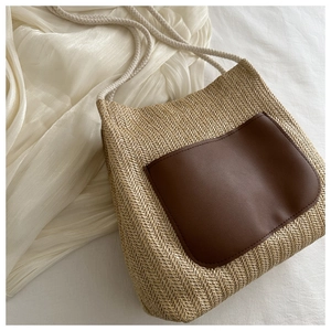 Detail of woven straw tote bag featuring brown leather front pocket and white cotton rope handle
