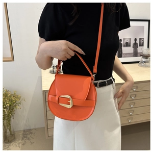Detail of bright orange saddle bag with gold horseshoe buckle on casual outfit