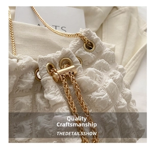 Macro detail of creamy white puff shoulder bag featuring pleated texture and gold metal chain