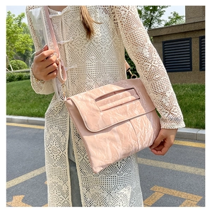 Vue détaillée de la texture plissée rose d'un sac brillant porté avec un cardigan en dentelle