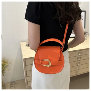 Detail of a bright orange saddle bag with gold buckle on a stylish wooden cabinet background