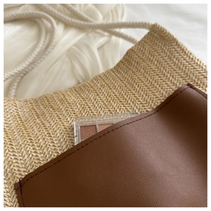 Close-up of woven straw tote bag with brown leather pocket and white rope handles