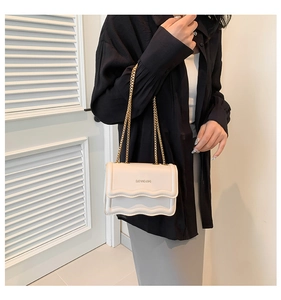Detail of cream white quilted bag featuring triple-layered wave flap and gold chain strap