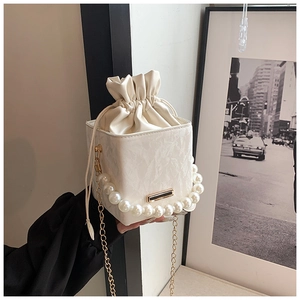 Detail of cream bucket bag with pearl handle, drawstring closure and gold chain strap