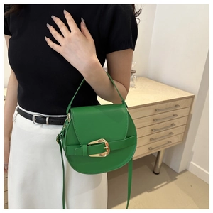 Green leather saddle bag with large gold buckle shown in a stylish crossbody carry style