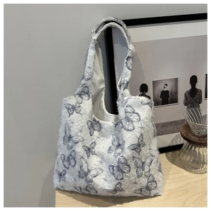 Detail of soft white plush tote bag with blue butterfly pattern on wooden tabletop
