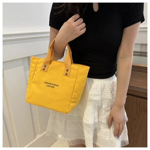 Detail of yellow canvas tote bag featuring leather text and metallic rivet accents