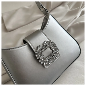 Close-up of silver faux leather shoulder bag with a large sparkling crystal buckle