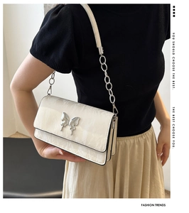 Detail of white textured underarm bag with silver butterfly buckle and chain strap